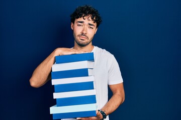 Sticker - Young hispanic man holding a pile of books depressed and worry for distress, crying angry and afraid. sad expression.