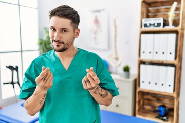 Canvas Print - Young physiotherapist man working at pain recovery clinic doing money gesture with hands, asking for salary payment, millionaire business