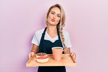 Poster - Beautiful young blonde woman wearing waitress apron holding breakfast tray looking at the camera blowing a kiss being lovely and sexy. love expression.