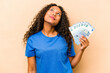 © Asier - Young hispanic woman holding bank notes isolated on beige background dreaming of achieving goals and purposes