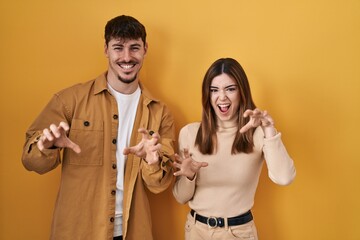 Sticker - Young hispanic couple standing over yellow background smiling funny doing claw gesture as cat, aggressive and sexy expression