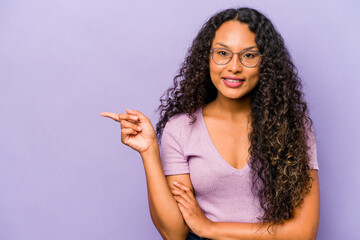 Wall Mural - Young hispanic woman isolated on purple background smiling cheerfully pointing with forefinger away.