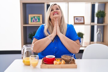 Sticker - Caucasian plus size woman eating breakfast at home begging and praying with hands together with hope expression on face very emotional and worried. begging.