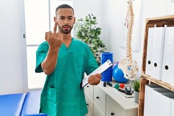 Poster - African american physiotherapist man working at pain recovery clinic showing middle finger, impolite and rude fuck off expression