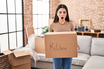 Sticker - Young woman moving to a new home holding box afraid and shocked with surprise and amazed expression, fear and excited face.