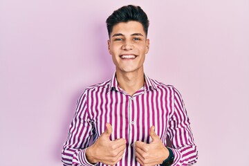 Sticker - Young hispanic man wearing casual clothes success sign doing positive gesture with hand, thumbs up smiling and happy. cheerful expression and winner gesture.