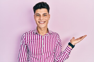 Sticker - Young hispanic man wearing casual clothes smiling cheerful presenting and pointing with palm of hand looking at the camera.