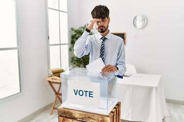 Poster - Hispanic man with beard voting putting envelop in ballot box worried and stressed about a problem with hand on forehead, nervous and anxious for crisis