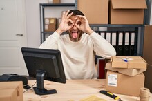 Handsome Middle Age Man Working At Small Business Ecommerce Doing Ok Gesture Like Binoculars Sticking Tongue Out, Eyes Looking Through Fingers. Crazy Expression.
