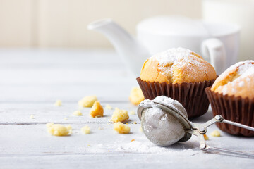 Freshly baked homemade muffins with powdered sugar and jug with milk on the wooden white table.