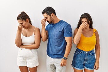 Wall Mural - Group of young hispanic people standing over isolated background tired rubbing nose and eyes feeling fatigue and headache. stress and frustration concept.