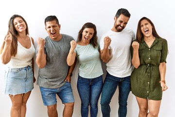 Wall Mural - Group of young hispanic friends standing together over isolated background very happy and excited doing winner gesture with arms raised, smiling and screaming for success. celebration concept.