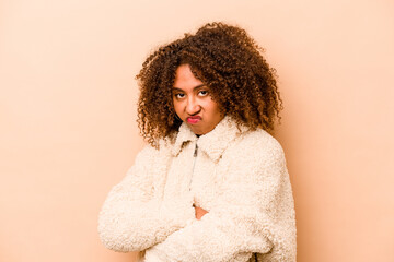 Young African American woman isolated on beige background frowning face in displeasure, keeps arms folded.