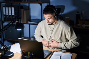 Canvas Print - Young handsome man working using computer laptop at night with hand on stomach because nausea, painful disease feeling unwell. ache concept.