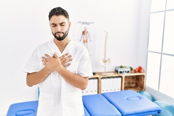 Sticker - Young handsome man with beard working at pain recovery clinic smiling with hands on chest with closed eyes and grateful gesture on face. health concept.