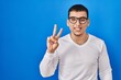 © Krakenimages.com - Young arab man wearing casual white shirt and glasses showing and pointing up with fingers number two while smiling confident and happy.