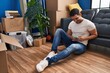 © Krakenimages.com - Young hispanic man using smartphone sitting on floor at new home