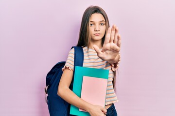 Sticker - Young brunette girl holding student backpack and books with open hand doing stop sign with serious and confident expression, defense gesture