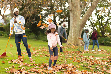 Image of happy african american multi generation family swiping leaves in autumn garden