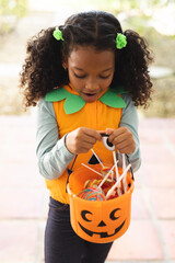 Vertical image of happy african american girl in halloween costume with basket