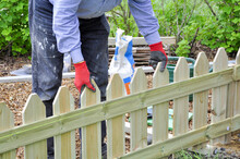 Background Of Hands Of Man In Red And Black Gloves Installing  A Wooden Fence In The Garden And Checking The Level With A Green String Over The Wooden Fence.