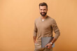 © Vadim Pastuh - Working with joy. Smiling cheerful business man wearing pullover sweater, standing with laptop, pc computer, looking at camera, isolated on beige background studio portrait
