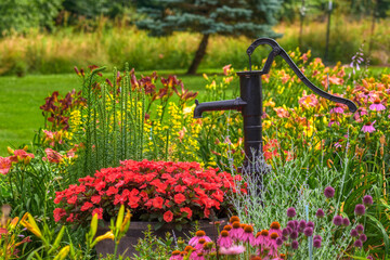 A hand water pump is in the middle of this beautiful home garden in PA.  Flowers surround this hand pump in a well-manicured Garden.