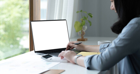 Wall Mural - Mockup image of a woman using laptop with blank white screen on wooden table in office