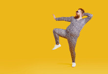 Funny Fat Fashion Guy In Pajamas Posing On Copy Space Background. Full Length Portrait Of Happy Joyful Plump Bearded Young Man Wearing Crazy Leopard PJs Dancing On Blank Yellow Copyspace Background