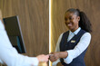 © pressmaster - Happy young black woman in uniform passing passport or keycard to male traveler over counter after registration of his personal data