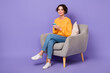 © deagreez - Full size portrait of positive nice person sit chair hold use telephone gadget isolated on purple color background