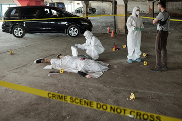 Wall Mural - Criminological expert in coveralls, mask, gloves and overboots communicating with policeman on crime scene