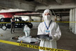 © pressmaster - Young female crime scene investigator in protective coveralls making notes in document while standing against colleague over dead body