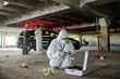 © pressmaster - Young female criminological expert in protective workwear looking for fingerprints of murderer on crime scene against two colleagues