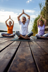 Wall Mural - Group of senior woman doing yoga exercises by the lake.