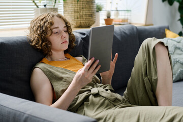 Aufkleber - Young relaxed Caucasian woman in casualwear looking through online data on screen of digital tablet while resting on couch at home