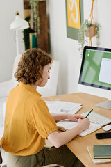 Aufkleber - Young businesswoman in casualwear making notes in notebook while sitting in front of computer monitor and planning work