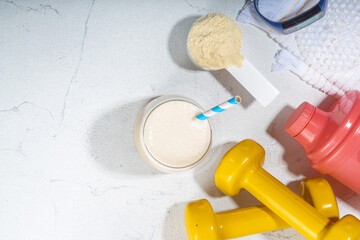 Vanilla white protein shake glass, with straw, with protein powder, dumbbell, towel and fitness accessories, on white sport bar table background copy space