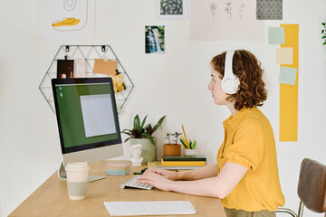 Aufkleber - Side view of young modern freelancer typing on computer keyboard while sitting in front of monitor with small blank window