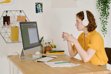 Aufkleber - Young serious female freelancer with cup of tea or coffee looking at computer screen with small blank window during work