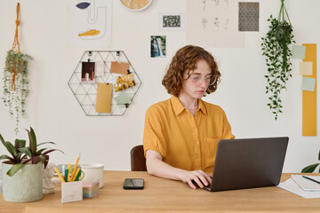 Aufkleber - Young student or freelancer in casualwear sitting in front of laptop by workplace at home and looking through online data on screen