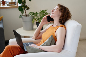 Aufkleber - Happy young businesswoman or home office manager with laptop sitting in comfortable armchair and speaking on mobile phone