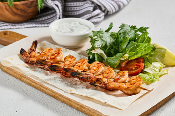 Canvas Print - Grilled shrimps with sauce on concrete background. Aesthetic composition with prawn skewer and fresh herbs. Shrimps on grill in summer menu. Seafood skewer in minimal style.