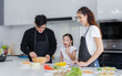 © atitaph - Happy family cooking together in the kitchen. Father, mother, and cute little daughter turn vegetables to make salads