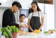 © atitaph - Happy family cooking together in the kitchen. Father, mother, and cute little daughter turn vegetables to make salads