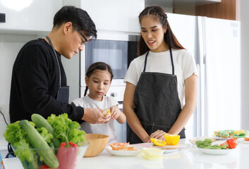 Sticker - Happy family cooking together in the kitchen. Father, mother, and cute little daughter turn vegetables to make salads