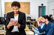 © ADDICTIVE STOCK - Content black worker browsing smartphone near colleagues