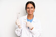 © kues1 - hispanic pretty woman smiling cheerfully, feeling happy and pointing to the side. dentist student concept
