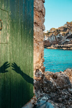 Hands Shadows On Aged Door Of Stone House On Rocky Beach In Sunlight