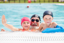 Joyful Kids With Grandfather Having Fun In Outdoor Swimming Pool